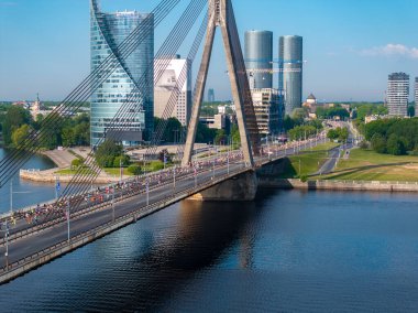 Riga, Letonya 'da belirgin bir üçgen kablo destekli köprüden geçen büyük bir kalabalığın hava görüntüsü. Arka planda şehrin ufuk çizgisi var..