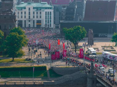 Riga, Letonya 'daki maraton koşucularının enerjisini yansıtan canlı bir hava çekimi. Sokaklar kırmızı bayraklar ve afişlerle dolu, olayları vurguluyorlar..