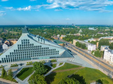 Riga 'daki modern üçgen Letonya Ulusal Kütüphanesi' ne kuşların bakış açısı, cam cephesi, bitişik park ve işlek sokak.