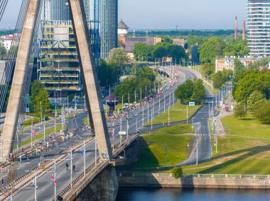 Riga, Letonya 'da benzersiz bir üçgen köprüye giden yolda büyük bir maraton koşucusu kalabalığını çekerken, arka planda bir nehir ve şehir manzarası vardı..