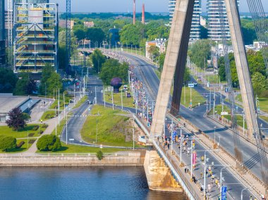 Riga, Letonya 'da eşsiz bir şekilde tasarlanmış bir köprünün üzerinde koşan maraton katılımcılarının hava görüntüsü. Arka planda şehir silüeti var..