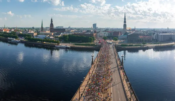 Riga, Letonya 'da bir nehirden geçen maraton katılımcılarının arka planda şehir manzaralı hava görüntüleri. Olayları ölçer ve güzellikleri kente çeker..