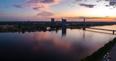 Gün batımında Letonya, Riga 'nın çarpıcı hava manzarası. Daugava Nehri, gökyüzünün canlı renklerini güzel bir şekilde yansıtır, gökyüzünün gökyüzünü aydınlatır..
