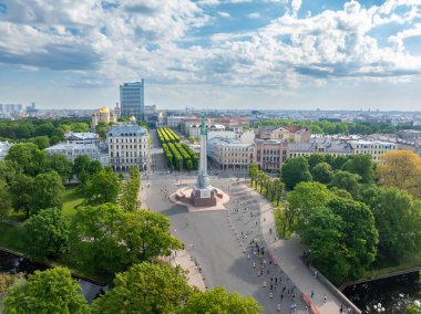 Letonya, Riga 'daki Özgürlük Anıtı' nın havadan çekimleri, maraton koşucuları geçerken. Anıt büyük bir kare ve yeşil ağaçlarla çevrili ve arka planda şehir silüeti bulunuyor..