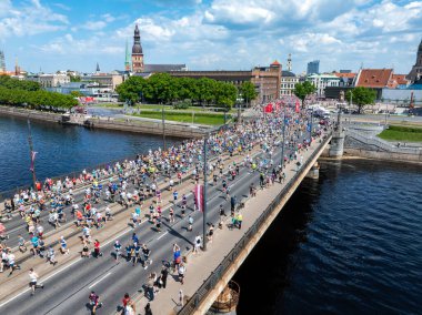 Riga, Letonya 'da bir nehirden geçen maraton koşucularının çarpıcı bir görüntüsü. Arka planda şehrin ufuk çizgisi var. Olayların boyutlarını gösteriyor..