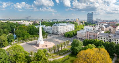 Riga, Letonya 'daki Özgürlük Anıtı' nın kuş bakışı manzarası, şehir manzarası ve arka planında binalar bulunan dairesel bir plaza ve park merkezli..