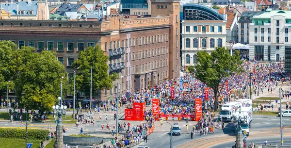 Riga Rimi Maratonu sırasında Riga sokaklarında koşan enerjik kalabalık. Görüntü her yaştan katılımcıları ve şehir mimarisini gösteriyor.