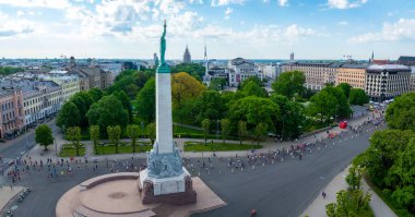 Letonya 'nın Riga kentindeki Özgürlük Anıtı' nın kuşbakışı manzarası, maraton katılımcılarıyla çevrili. Arkaplanda binalar ve ağaçların olduğu şehir manzarası görülebilir..