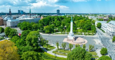 Riga, Letonya 'daki Özgürlük Anıtı' nın kuş bakışı manzarası. Etrafı yemyeşil ve yürüyen insanlarla çevrili. Riga şehrinin manzarası arka planda görünür..