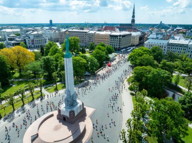 Riga, Letonya 'da canlı Riga Rimi Maratonu 2024' ü kaydeden hava çekimi. Koşucular şehrin sokaklarını belirgin bir şekilde görünen ikonik Özgürlük Anıtı ile doldurdu..