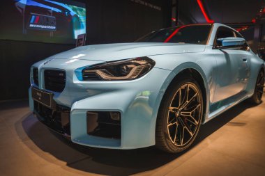 Açık mavi bir BMW M2 yarışma arabası, kapalı mekanda keskin farlar, siyah ızgara ve şık alaşımlı tekerleklerle sergileniyordu. İyi aydınlatılmış sergi salonu parlak sonunu geliştirir..