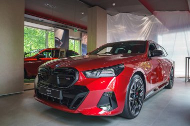 Parlak kırmızı bir BMW i5 dışarıda büyük pencereleri ve yeşilliği olan minimalist bir galeride sergileniyordu. Profesyonel ortamda, muhtemelen Londra, İngiltere 'de olmak üzere başka bir araç ve tanıtım materyalleri yer alıyor..