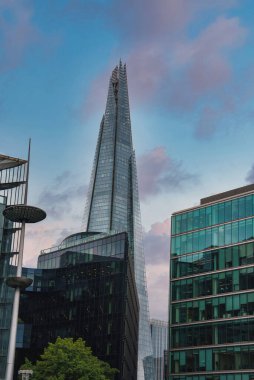 Çömlek parçası bulutlu bir gökyüzüne karşı dimdik ayakta duruyor, modern ofis binalarıyla çevrili, yansıtıcı cam pencereleri ve Londra, İngiltere 'de yeşillik dokunuşuyla..