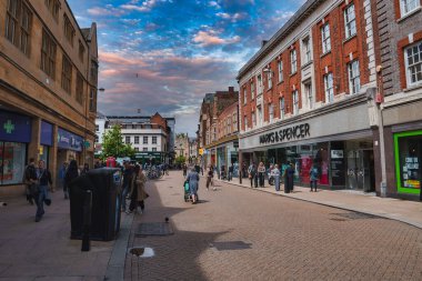 Cambridge, İngiltere 'de canlı bir caddede tarihi mimari, Marks and Spencer mağazası ve alışveriş yapan insanlar var. Parçalı bulutlu gökyüzü, canlı sahneye cazibe katar..