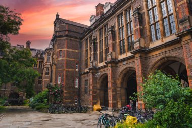 Cambridge, İngiltere 'de güzel tarihi bir bina, kırmızı tuğla ve taş mimarisi, geniş kemerli pencereler, ve gün batımında park halindeki bisikletlerle sakin bir bahçe..