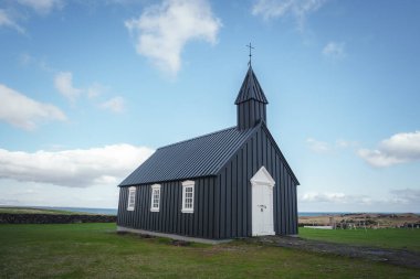 Budir, İzlanda 'daki ikonik Budakirkja siyah kilisesi, açık mavi gökyüzüne ve çimlerle çevrili dağınık bulutlara karşı eşsiz mimarisiyle göze çarpıyor..