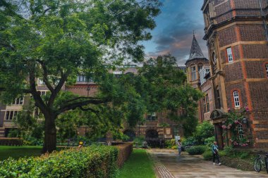 Cambridge, İngiltere 'de sakin bir avlu, yemyeşil, kemerli pencereli kırmızı tuğlalı binalar, sivri uçlu bir taret ve kaldırım taşı patikası var..