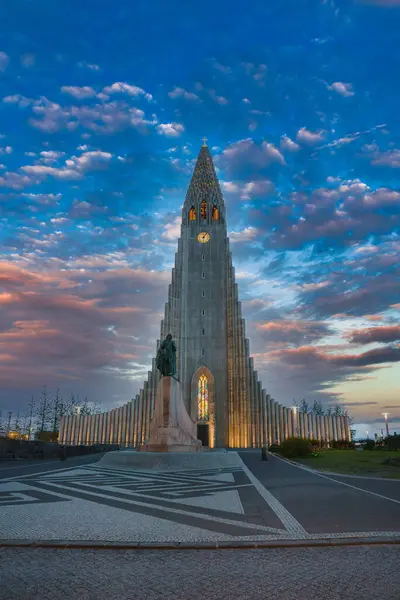 Hallgrimskirkja kilisesinin çarpıcı mimarisi, Reykjavik, İzlanda 'daki Leif Erikson heykeliyle alacakaranlıkta aydınlandı. Titrek gökyüzü dramatik bir etki yaratıyor.