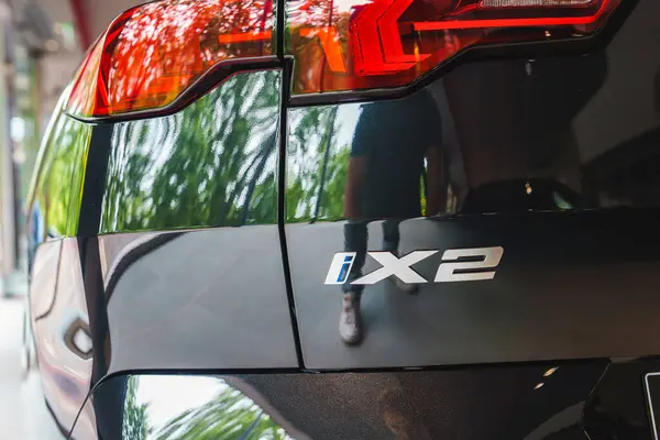 stock image Close-up of the rear section of a black BMW iX2, showcasing its distinctive taillight design. Reflections of greenery and a person suggest an outdoor setting in London, UK.