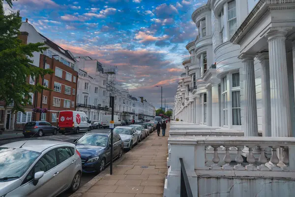 stock image A serene street in London, UK, featuring classic white terraced houses with ornate columns and railings. A red DPD delivery van adds a modern touch to the historic setting.