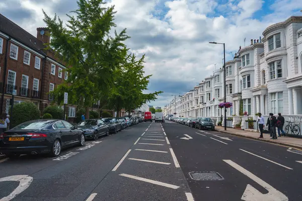 stock image A picturesque street in London, UK, featuring a mix of traditional brick buildings and elegant white terraced houses. A red double-decker bus and pedestrians add to the citys charm.