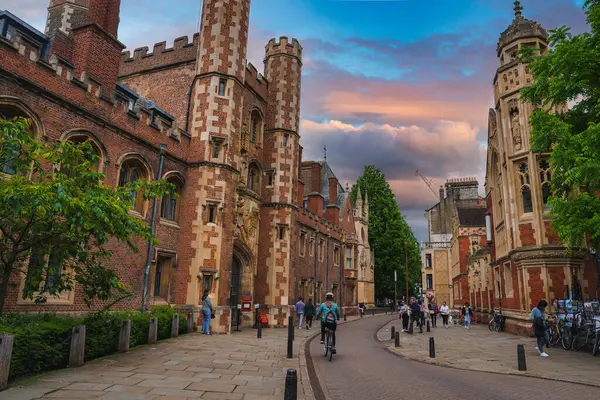 Stock image Picturesque street in Cambridge, UK, featuring historic Gothic buildings, an ornate entrance gate, and a lively atmosphere with pedestrians and cyclists.