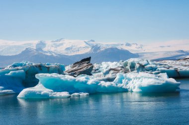İzlanda 'daki Jokulsarlon Buzul Gölü' nün göz kamaştırıcı manzarası. Mavi renkli buzdağları ve parlak mavi gökyüzünün altındaki görkemli Vatnajokull buzulları..