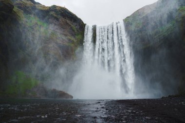 İzlanda 'daki Skogafoss şelalesi güçlü akışını ve etkileyici yüksekliğini, yosun kaplı kaya ve sisle çevrelenmiş, dramatik ve ruhani bir atmosfer yaratarak sergiliyor..