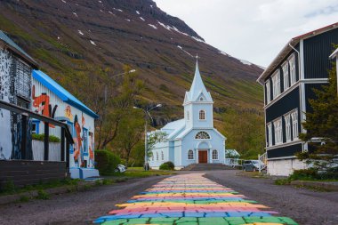 Seydisfjordur, İzlanda 'daki Picturesque caddesinde uzun bir çan kulesi, canlı duvar resimleri ve bir dağ zeminine karşı gökkuşağı boyalı bir patika var..