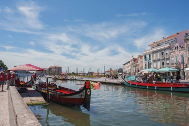 Portekiz, Aveiro 'da büyüleyici bir kanal, güneşli bir günde geleneksel moliceiros, pastel renkli binalar ve açık hava oturma alanları sunuyor..