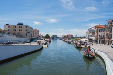 Portekiz, Aveiro 'nun renkli binalar ve geleneksel moliceiro tekneleriyle dolu canlı bir manzarası. Açık gökyüzü ve canlı yayalar cazibesini arttırıyor..