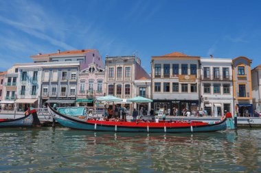 Portekiz 'in Aveiro şehrinde, kenetlenmiş bir Moliceiro teknesiyle bir kanal boyunca canlı geleneksel binaların yer aldığı görkemli bir manzara. Açık mavi gökyüzü cazibeme yenisini katıyor.