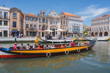 Portekiz 'in Aveiro şehrinde turistlerle dolu, kafeler ve dükkanlarla dolu, açık mavi gökyüzünün altında renkli moliceiro teknelerinin yer aldığı canlı bir manzara..