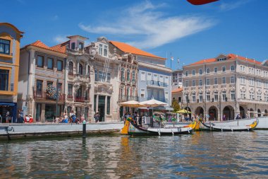 Renkli binalar ve molisirolar ile kaplı Aveiros kanalının büyüleyici manzarası. İnsanlar açık mavi gökyüzünün altındaki açık kafelerin keyfini çıkarırlar, şehrin canlı atmosferini yansıtırlar..