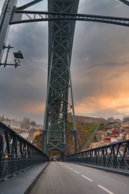 Porto, Portekiz 'deki Dom Luis Köprüsü' nün alt güvertesinden, karmaşık demircilik, dramatik bir gün batımı gökyüzü ve canlı yamaç mimarisi..