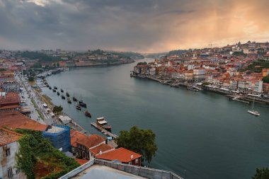 Portekiz, Porto 'daki Douro Nehri' nin çarpıcı manzarası. Ribeira 'da renkli binalar ve dramatik bir gökyüzü altında geleneksel Rabelo tekneleri yer alıyor..
