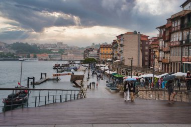 Portos 'un Douro Nehri' ne bakan manzarası, renkli tarihi binalar ve dramatik bir gökyüzünün altında gezinen insanlar..