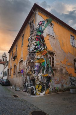 Portekiz 'in Porto kentindeki eski sarı bir binada geri dönüşümlü malzemelerden yapılmış büyük bir tavşan heykelinin yer aldığı canlı bir sokak sanatı kurulumu. Çakıl taşı caddesi ve kilise kulesi arka planda..