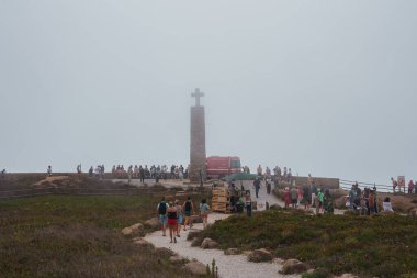 Portekiz, Cabo da Roca 'da puslu bir manzara, haçlı uzun bir taş heykel, sayısız ziyaretçi ve satıcı tezgahı olan engebeli bir manzara..