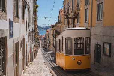 Çekici sarı bir tramvay Lizbon, Portekiz 'de dik ve dar bir caddede yol alır. Geleneksel balkon ve pastel cepheli binalar kaldırım taşı caddesi hizasında.