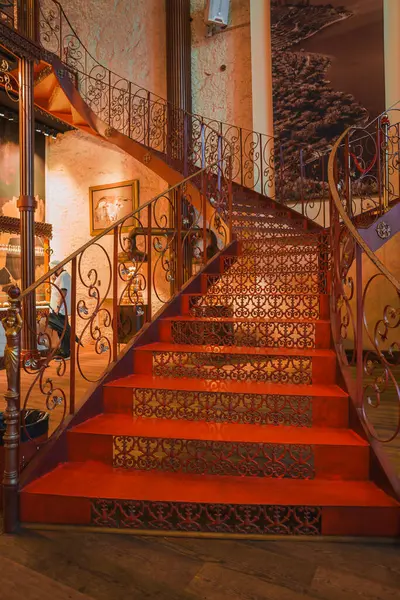 stock image Elegant staircase with intricate wrought iron railings and red carpeted steps inside a culturally significant building in Porto, featuring warm-toned walls and framed artwork.