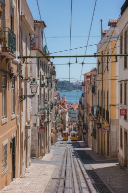 Lizbon, Portekiz 'deki pitoresk bir caddede geleneksel sarı tramvaylar, balkonları olan canlı çok katlı binalar ve Tagus Nehri manzarası var..
