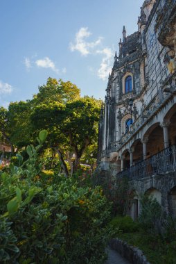 Quinta da Regaleira 'nın süslü taş oymalarını ve kemerli pencerelerini keşfedin, yemyeşil bahçelerle çevrili ve açık mavi gökyüzünün altında güneşle yıkanmış..