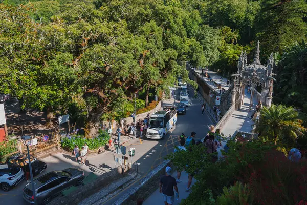 Portekiz, Sintra 'da canlı bir cadde, Quinta da Regaleira' nın süslü giriş kapısı. Turistler ve araçlar verimli yeşilliklerle çevrili dar yolda ilerliyorlar.