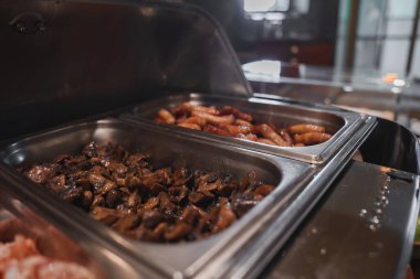 Lüks otellerin açık büfesinde sotelenmiş mantarlar ve paslanmaz çelik çalı tabaklarında çeşitli sosisler var. Ortam aydınlatmalı sofistike bir iç mekan..