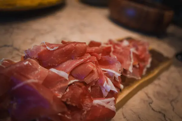 stock image Elegant presentation of thinly sliced prosciutto on a wooden board, set against a marble countertop, highlighting the luxury and attention to detail in upscale dining.