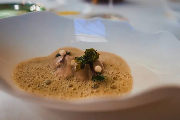 stock image A beautifully plated gourmet dish with frothy sauce and delicate garnishes in a luxury hotel. The elegant table setting and blurred background enhance the ambiance.