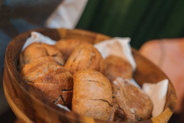 Taze pişmiş ekmek ruloları, altın-kahverengi kabuk ve ahşap bir kâsede kırsal görünüm, rahat ve lüks bir yemek deneyimi olduğunu gösteriyor..
