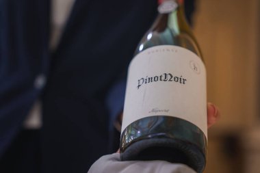 Resmi giyinmiş bir garson tarafından sunulan Pinot Noir şarap şişesinin zarif bir sunumu güzel bir yemek restoranının lüks ve sofistike atmosferini vurguluyor..