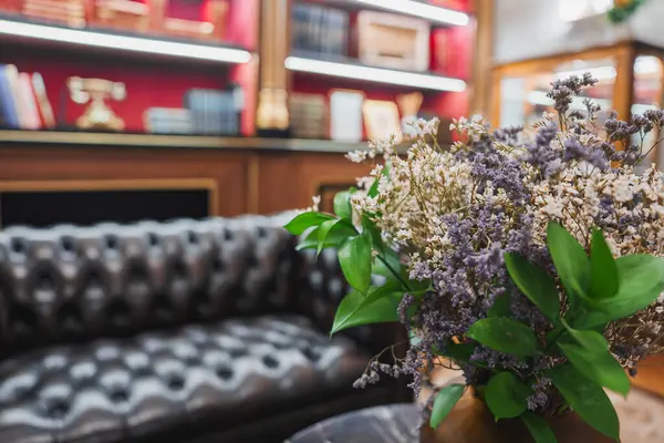 stock image Elegant hotel interior featuring a plush leather sofa, illuminated wooden bookshelves, and a bouquet of dried flowers, showcasing luxury and sophisticated decor.